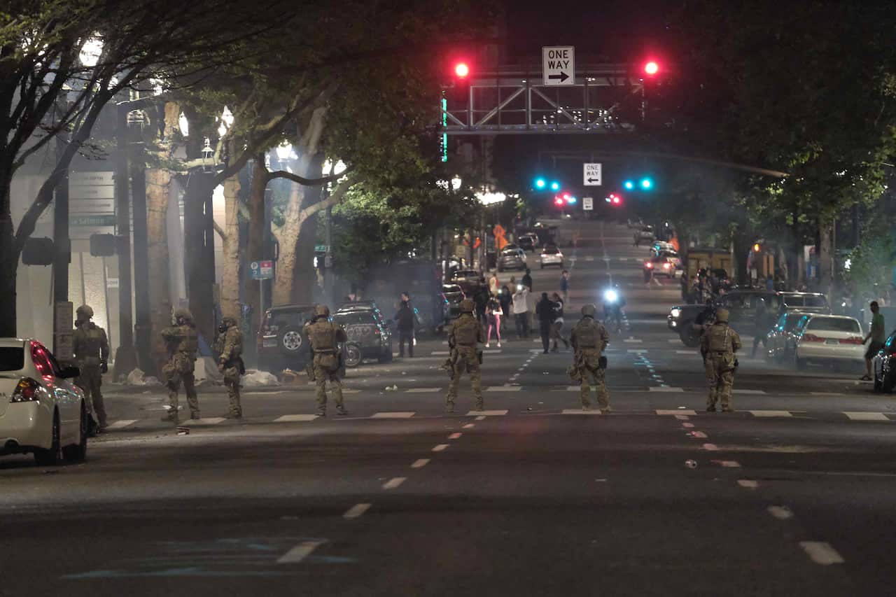 Federal officers block a street after launching a round after tear gas at protesters who removed fencing around entrance to the federal courthouse in Portland.