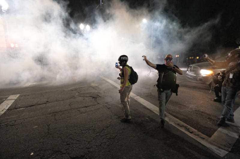 People identifying as press record the scene as federal officers launch tear gas