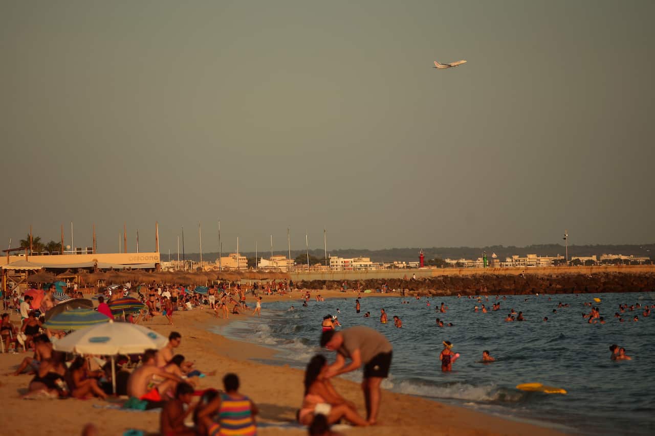 People enjoy the beach as an airplane takes off from the Balearic Islands capital of Palma de Mallorca, Spain. 