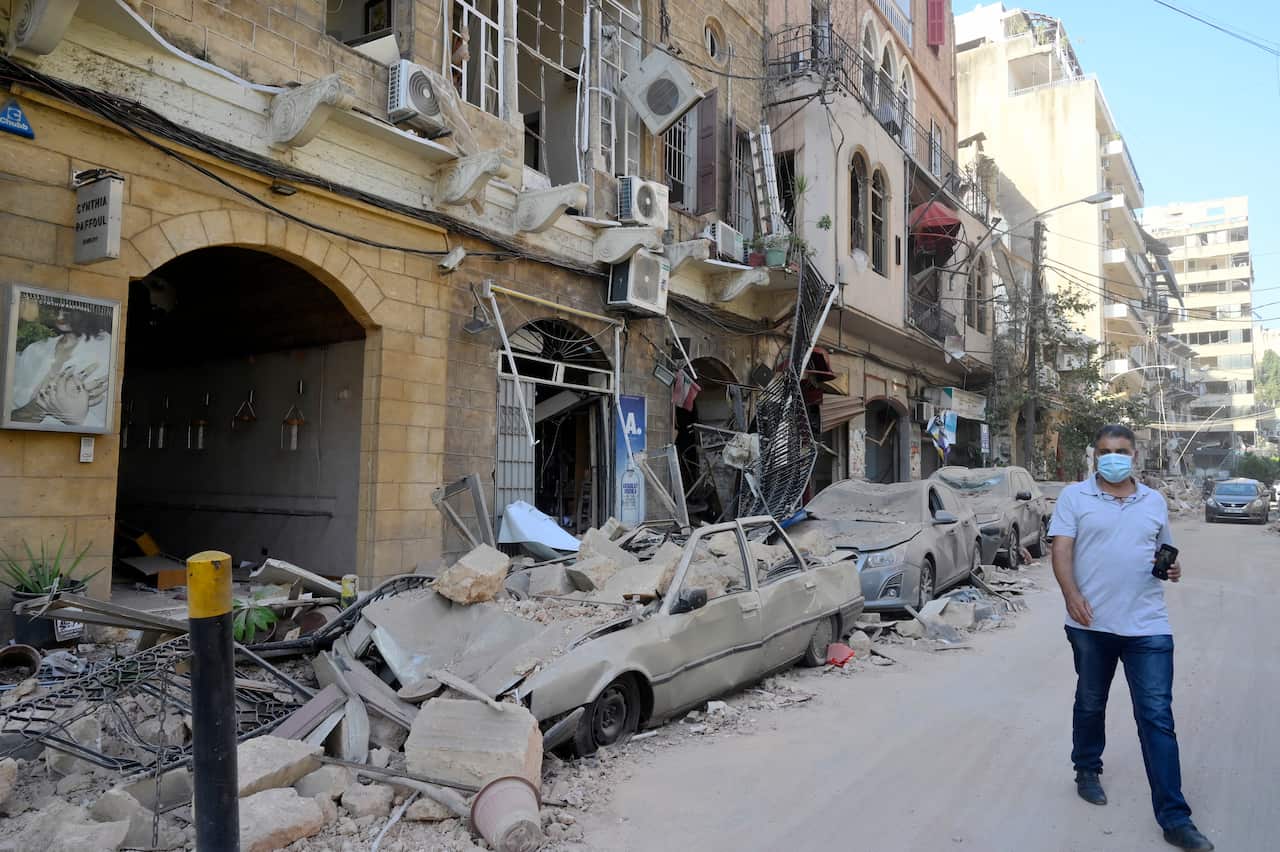 A man walks next to damaged vehicles in the aftermath of a massive explosion in Beirut.