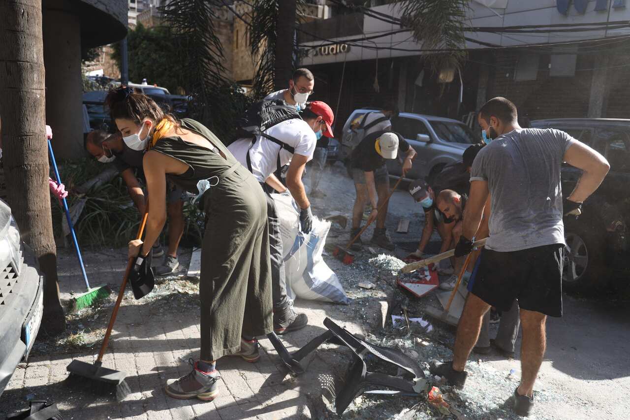Lebanese youth clear glass debris in a street, one day after an explosion at the Beirut Port.
