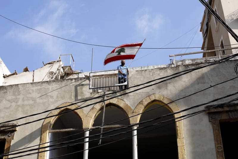 A man puts a Lebanese flag on a roof of a damaged building