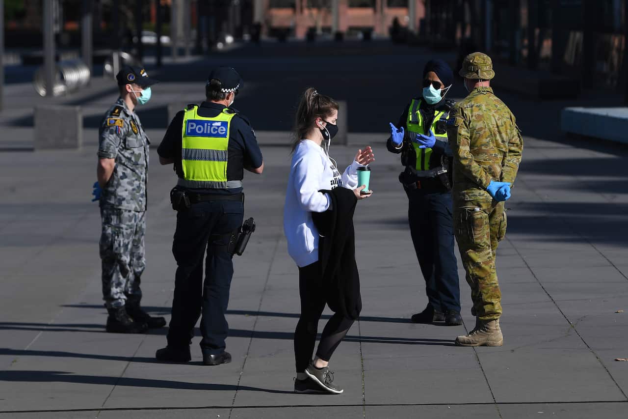 A person wearing a face mask walks past Victoria Police, Airforce and ADF personnel outside of the Melbourne Museum in Melbourne.