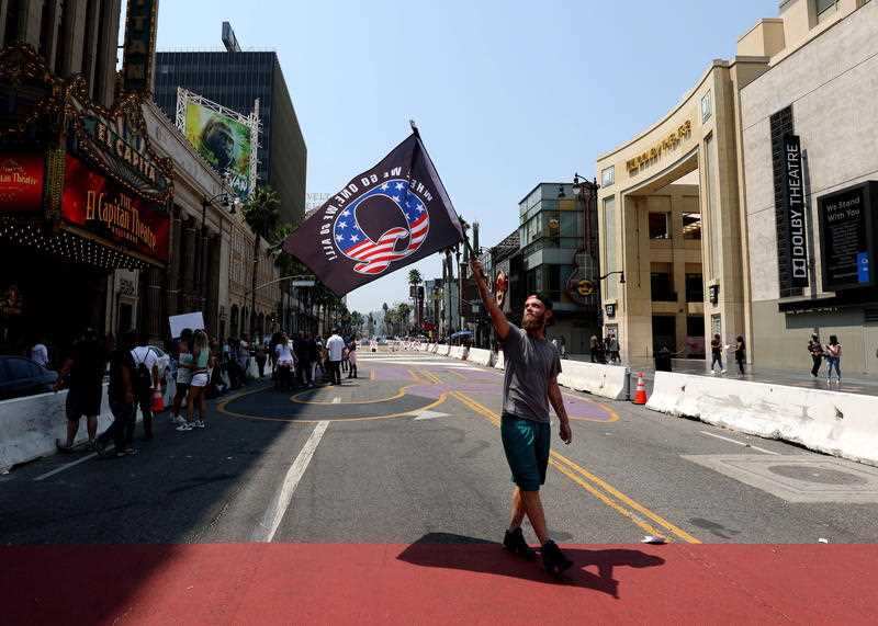A man holds a QAnon conspiracy flag while walking over the All Black Lives Matter mural in Hollywood.