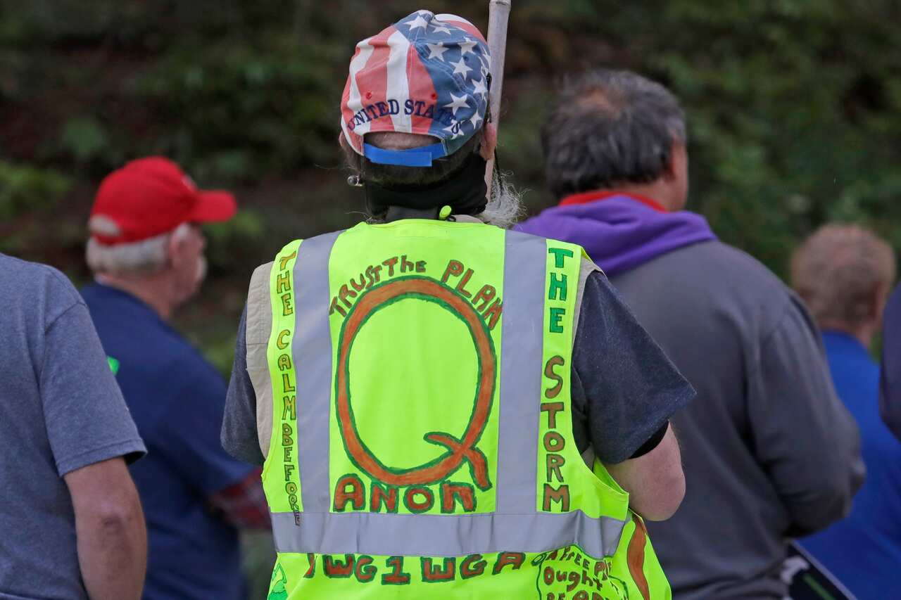 In this May 14, 2020, file photo, a person carries a sign and wears a vest supporting QAnon at a protest in Olympia, Washington 