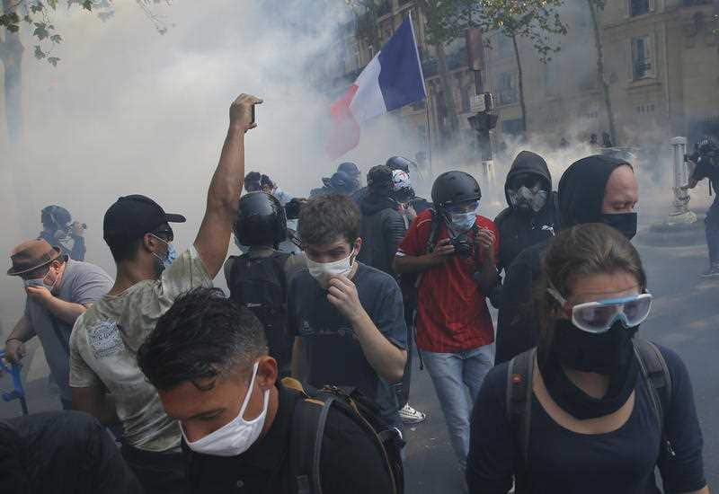 Yellow vest protesters escape tear gas fired by French police while wearing protective face masks as precaution against the conoravirus during a march in Paris.