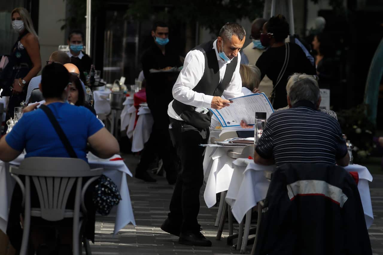 A waiter serves customers as they dine out in London.