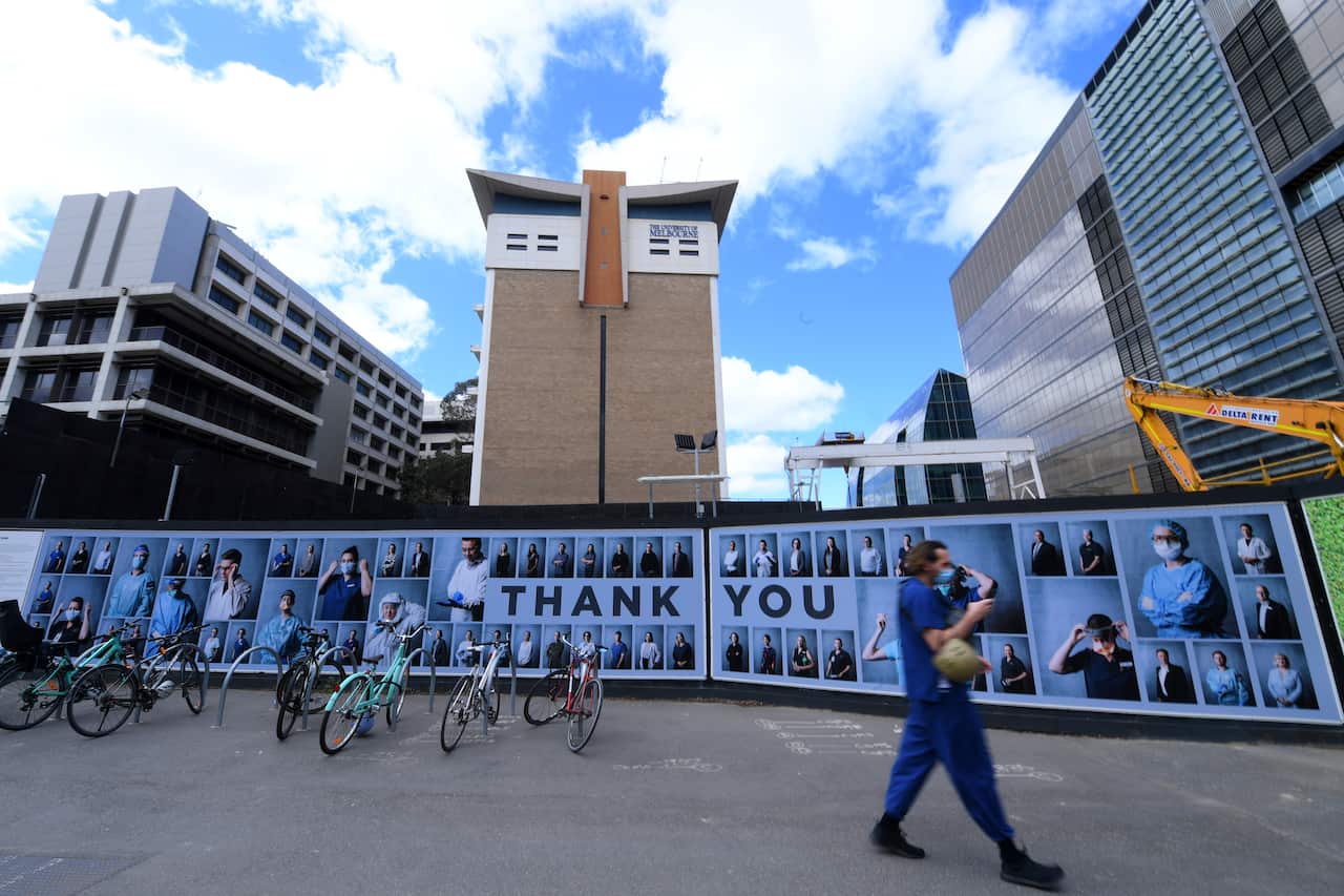 People wearing face masks walk past an outdoor photography exhibition of healthcare workers in Melbourne.