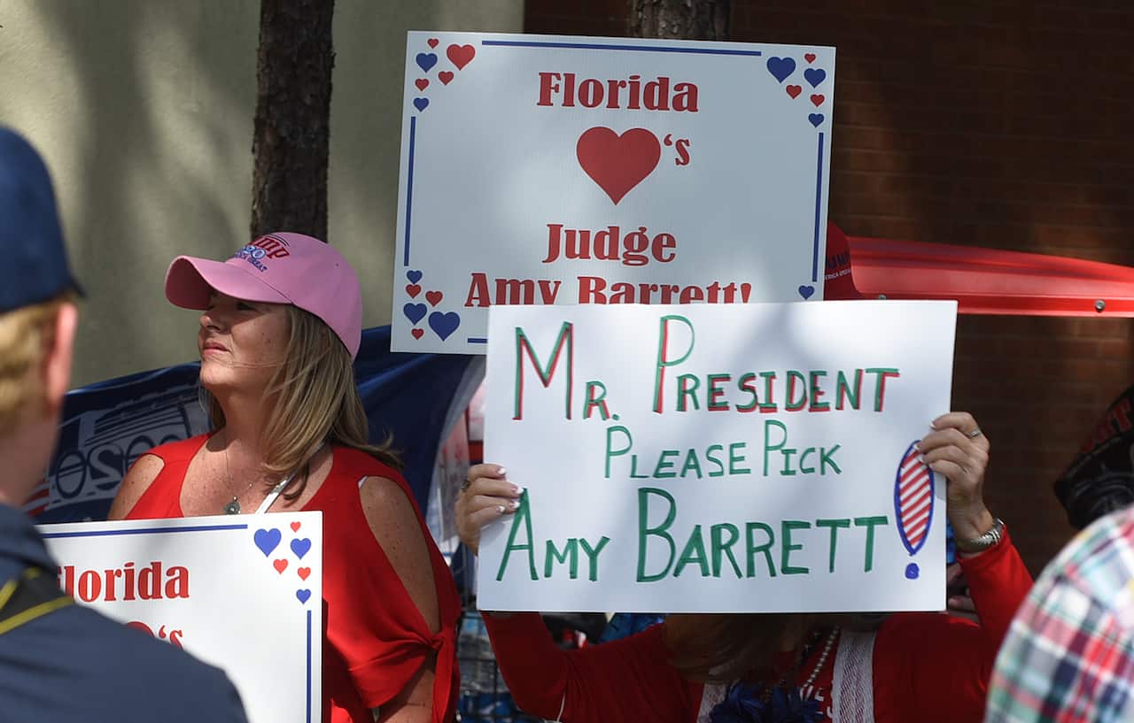 People hold placards in support of Judge Amy Coney Barrett, as supporters of US President Donald Trump arrive at a Jacksonville campaign rally.