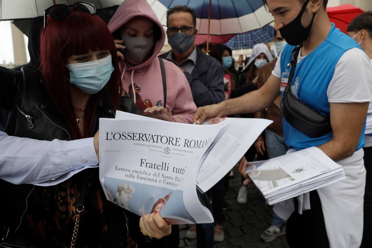 Copies of L'Osservatore Romano with the Pope Francis encyclical are distributed by volunteers.