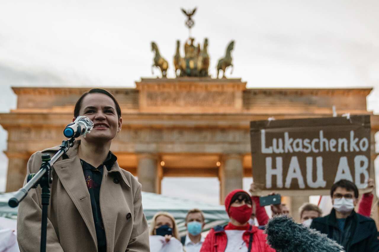 Belarusian opposition leader Sviatlana Tsikhanouskaya (L) speaks during a protest against the political situation in Belarus, as a protesters raises a cardboard reading ’Lukashenko get lost'.