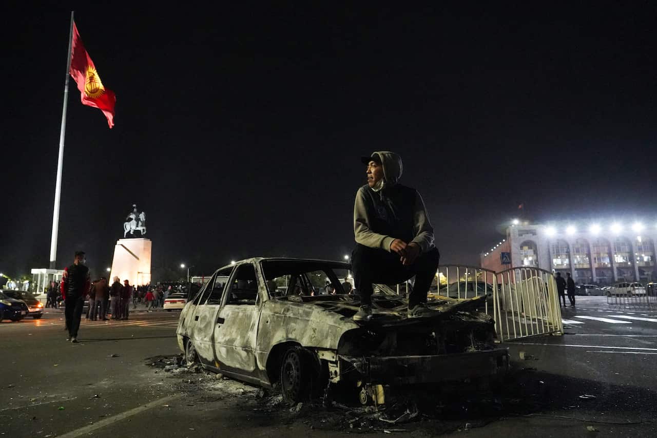 A man sits on a burned out vehicle in central Bishkek