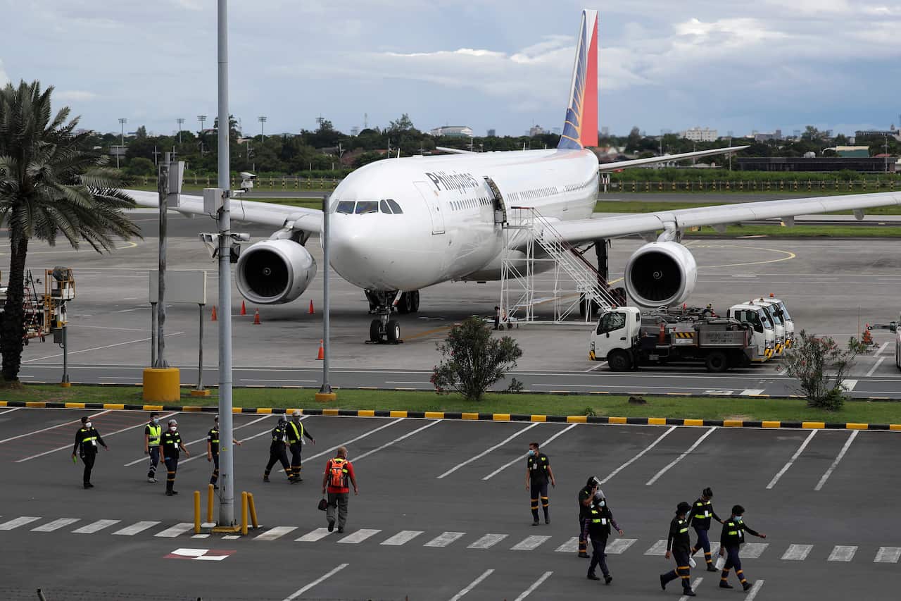 Airport workers walk in front of a Philippine Airline plane at Manila's airport