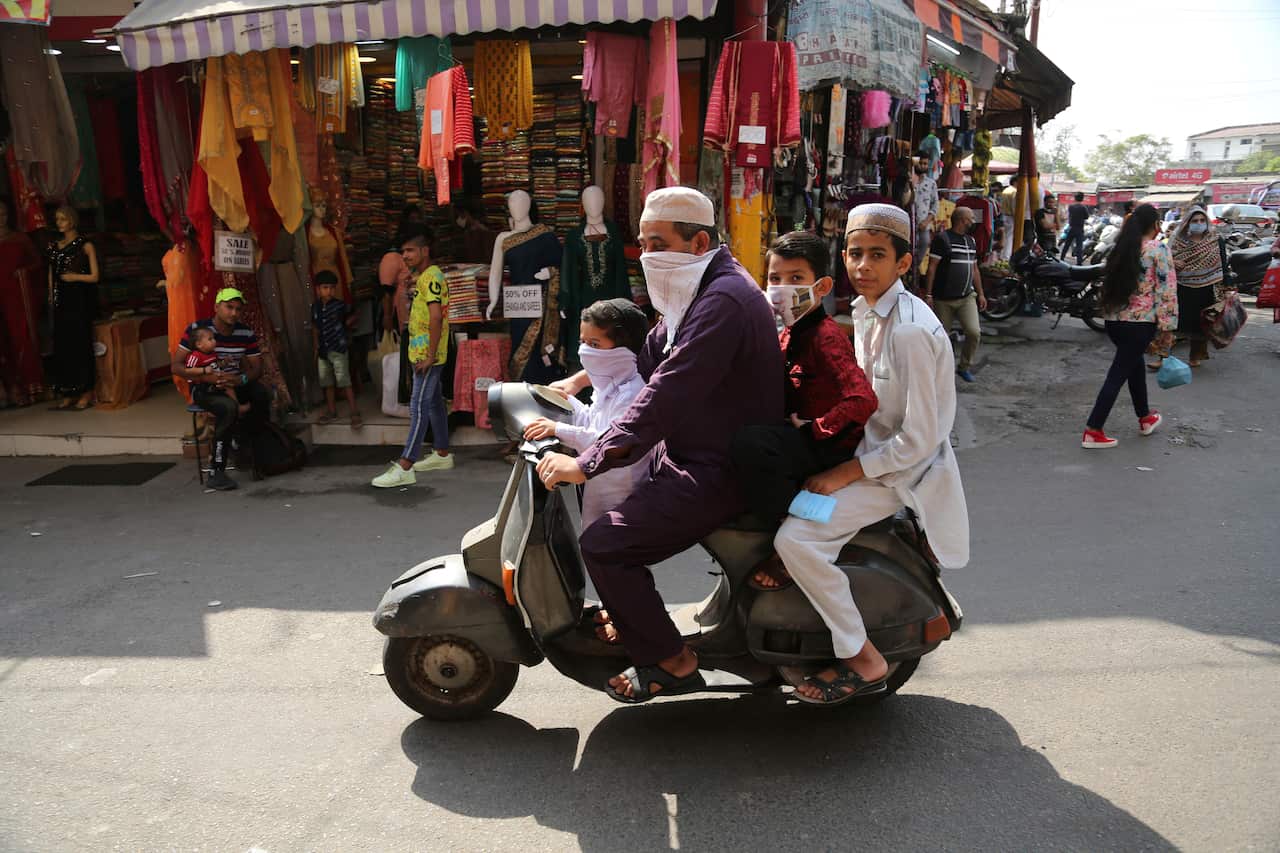 Indian man wearing face mask as a precaution against the coronavirus ride scooter with children at market in Jammu, India
