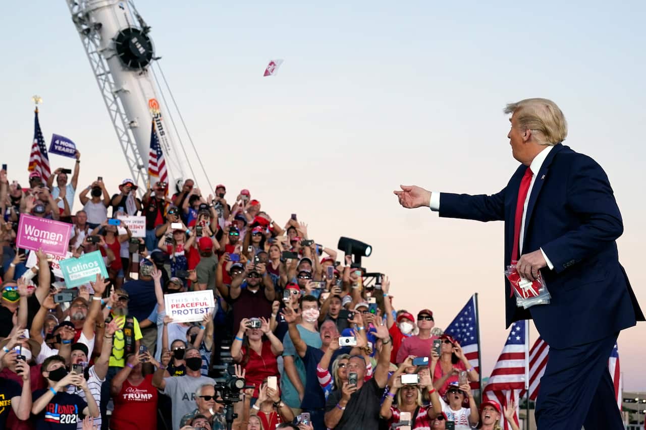 President Donald Trump throws face masks into the crowd as he arrives at the campaign rally on Monday.