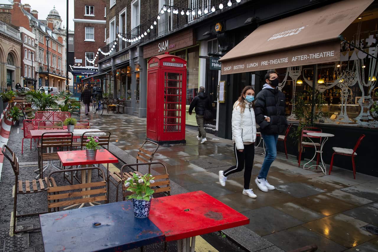 People wearing face masks walk pass empty tables outside bars and restaurants in Covent Garden, in central London.