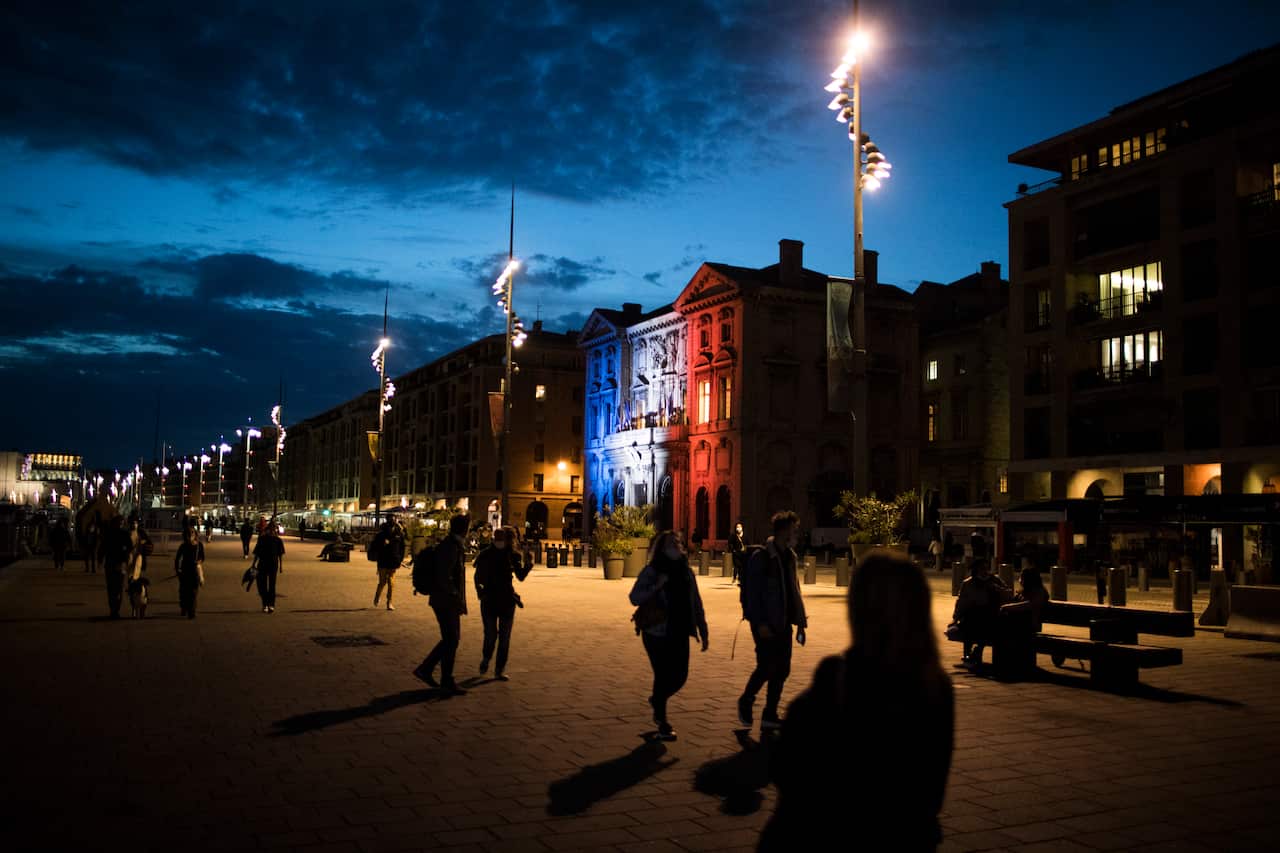Pedestrians walk along Marseille's Old Port as the town hall is lit up in the French Tricolor to honor slain teacher Samuel Paty, Wednesday, 21 October, 2020. 