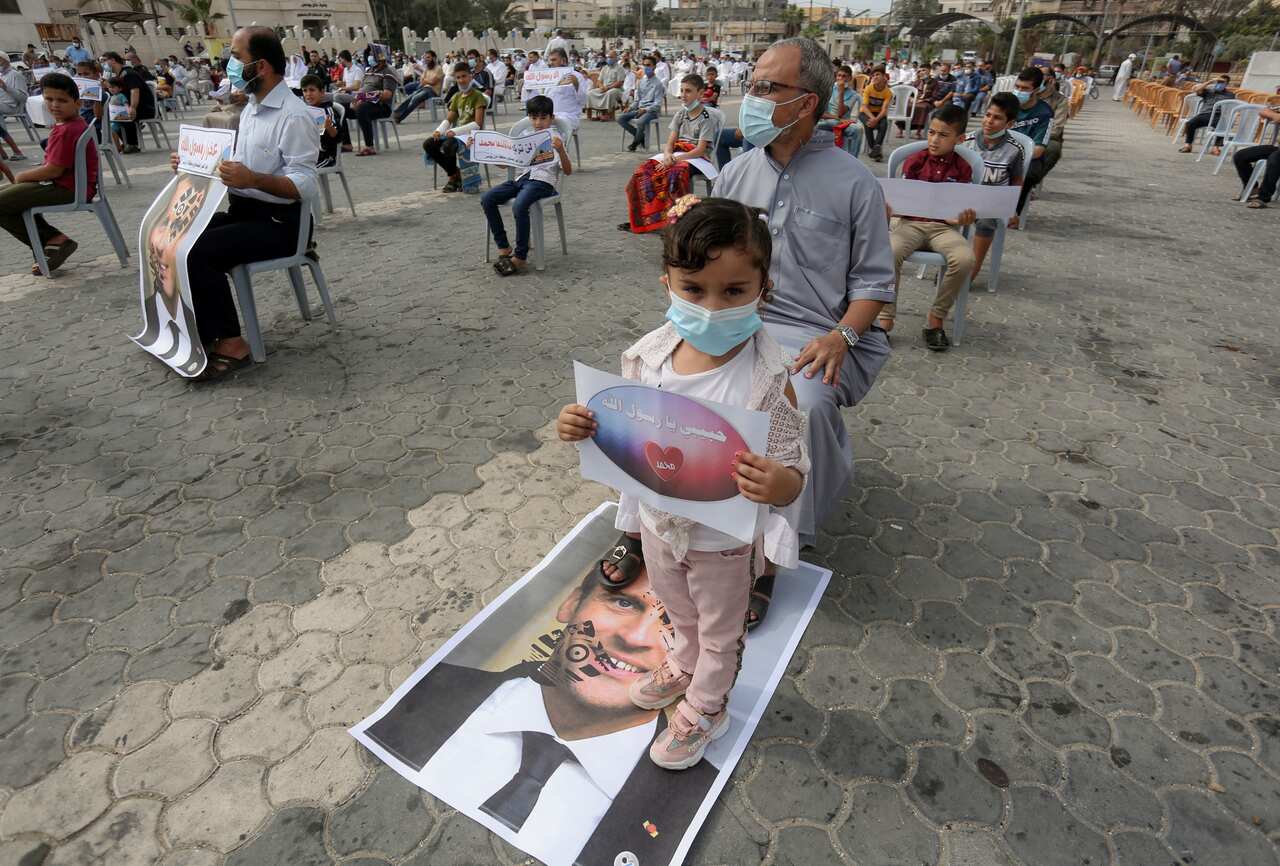 A Palestinian child wearing a face mask stands on a placard with a picture of the French President Emmanuel Macron during the protest
