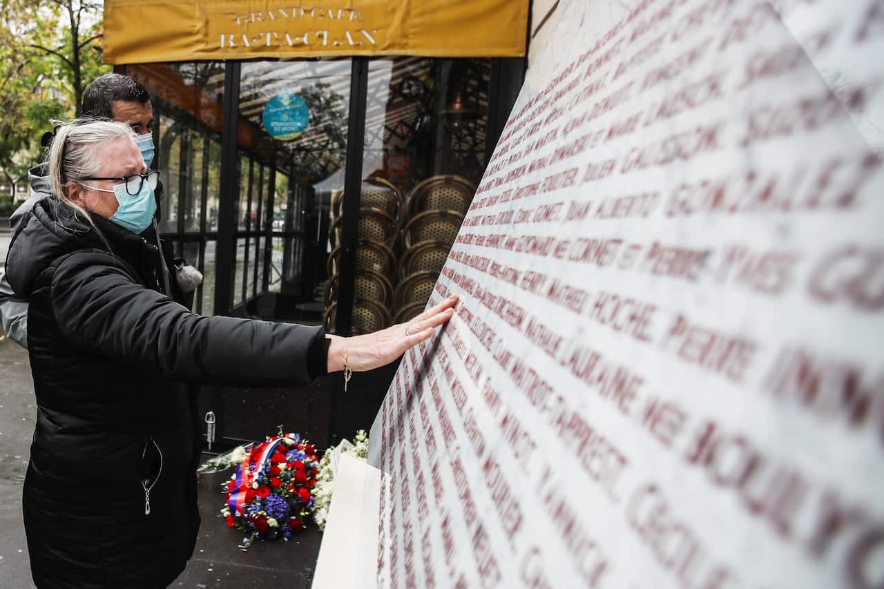 A woman touches the memorial stone after she put flowers outside the Bataclan concert venue, a site of the terror attacks, in Paris, France, 13 November 2020.