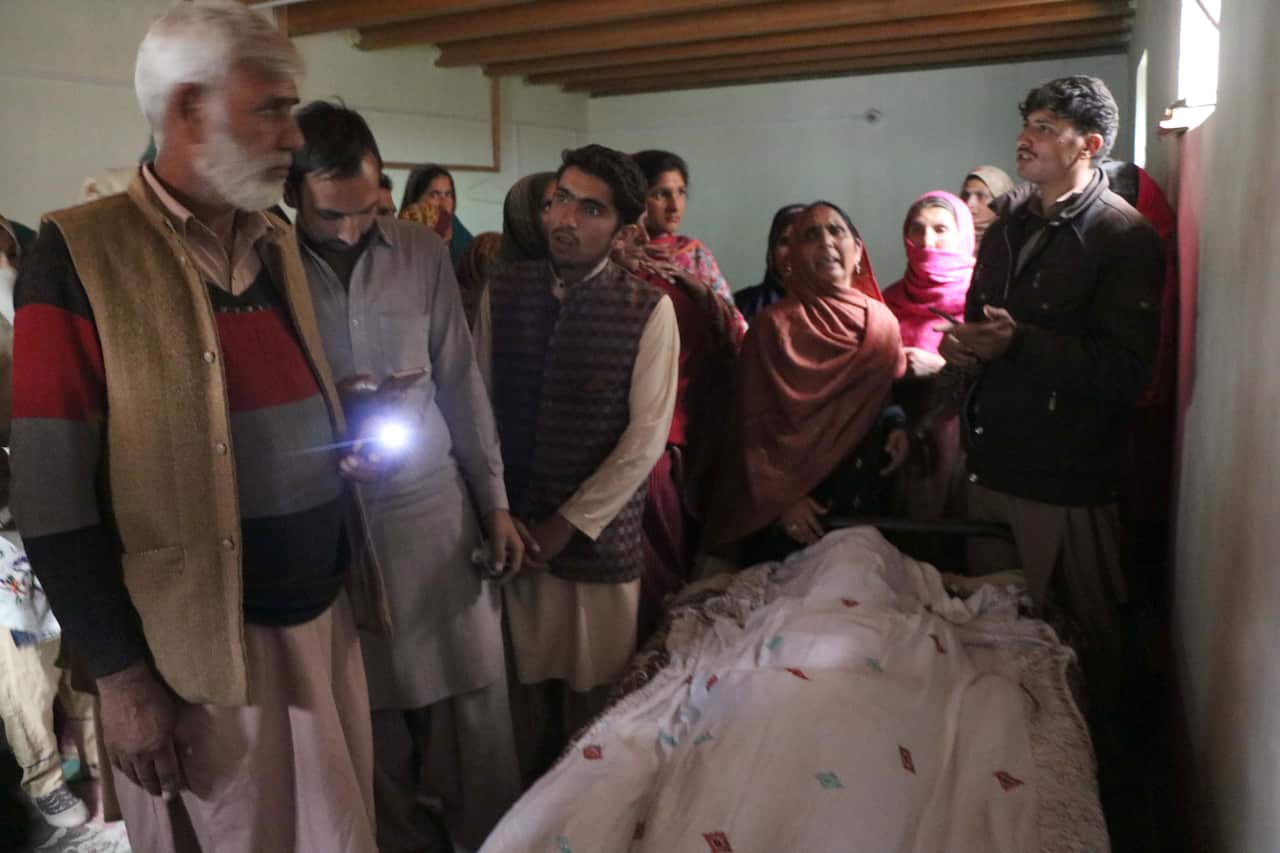 Relatives sit beside the body of a victim who was killed allegedly by the Indian forces firing between Pakistani and Indian administered Kashmir