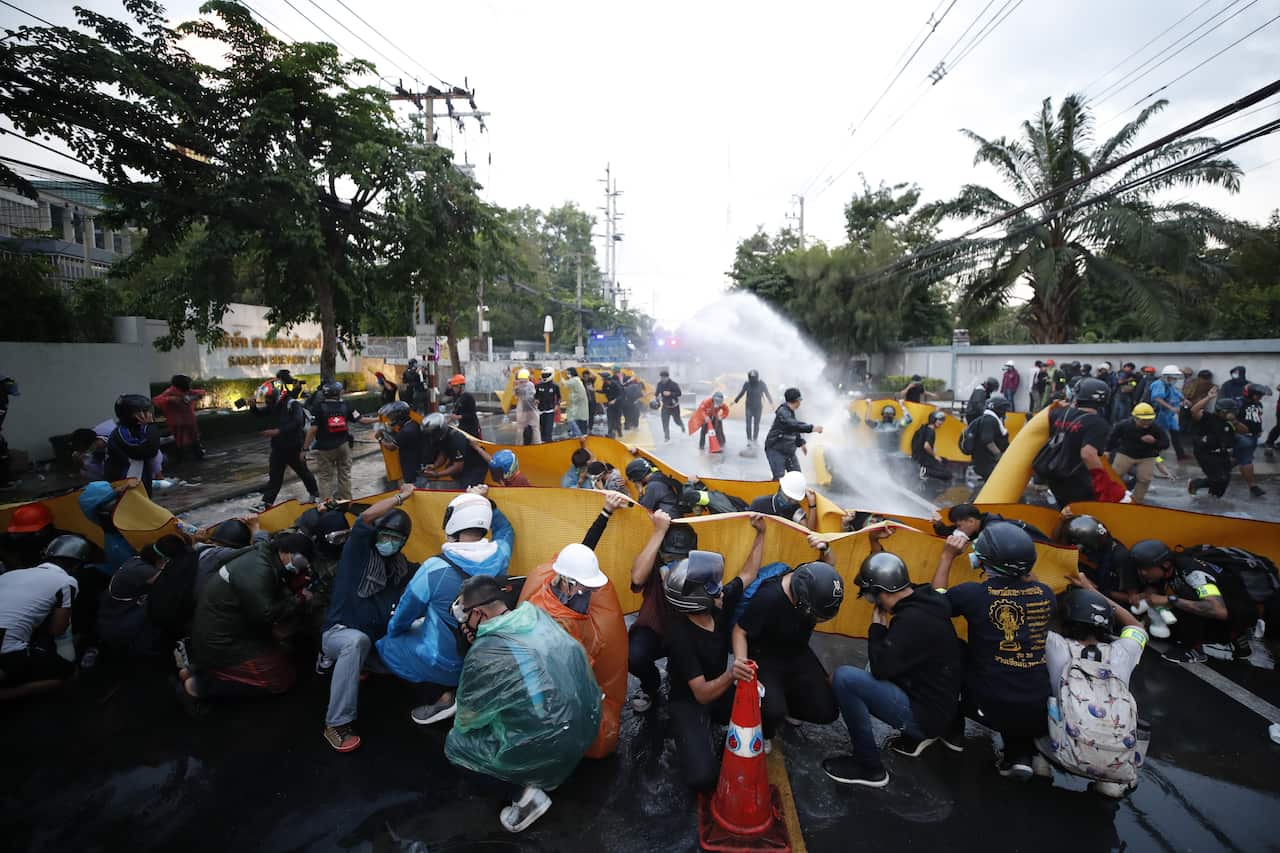 Pro-democracy protesters take cover as police fire tear gas and water cannon during a demonstration against a charter amendment at Parliament in Bangkok