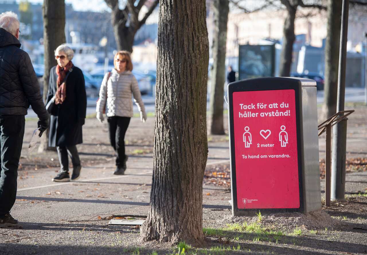 People strolling in Stockholm pass a sign asking to maintain social distancing, amid the continuous spread of the coronavirus disease.