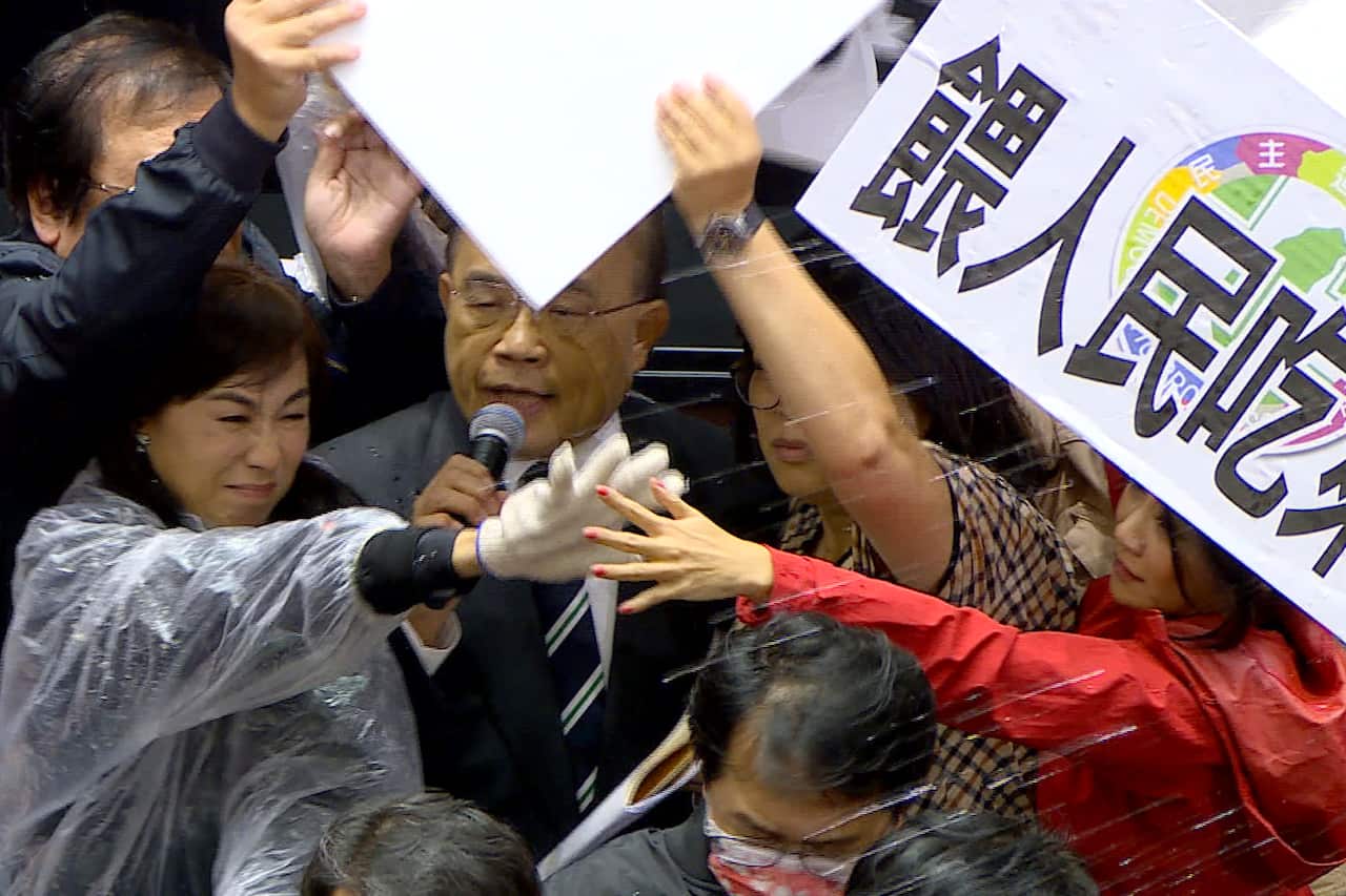 Taiwanese Premier Su Tseng-chang holds a microphone as opposition party lawmakers from the Nationalist party block his attempt to speak. 