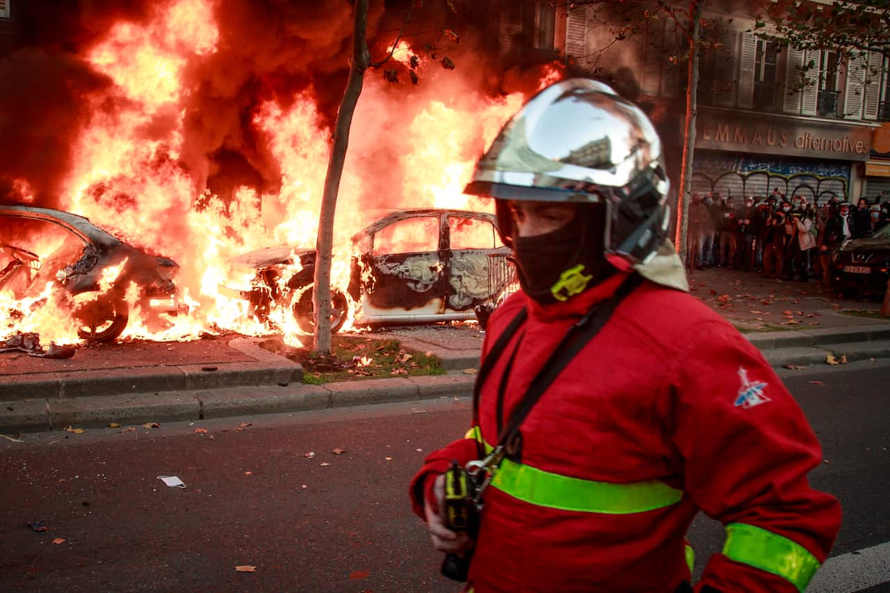 Firefighters extinguish a burned car as clashes erupt at Bastille Square after a demonstration against the newly passed controversial global security law in Paris, France.