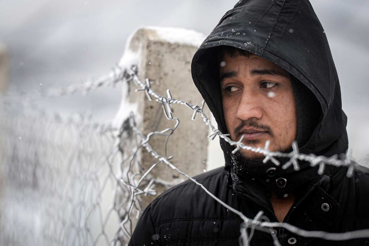 A migrant stands next to a fence during snowfall by the Lipa camp, outside Bihac, Bosnia