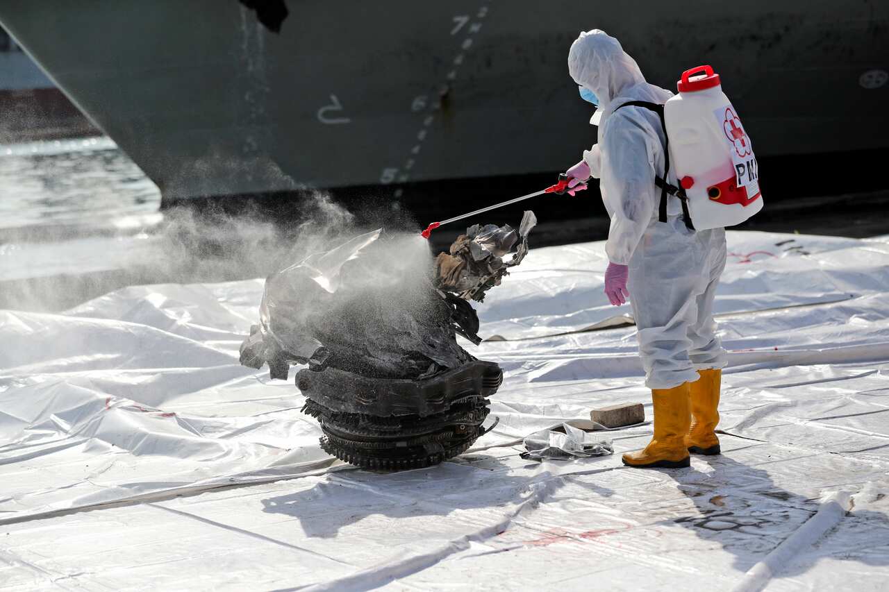 A health worker sprays disinfectant at a large part of aircraft recovered from the waters off Java Island where Sriwijaya Air flight SJ-182 crashed.