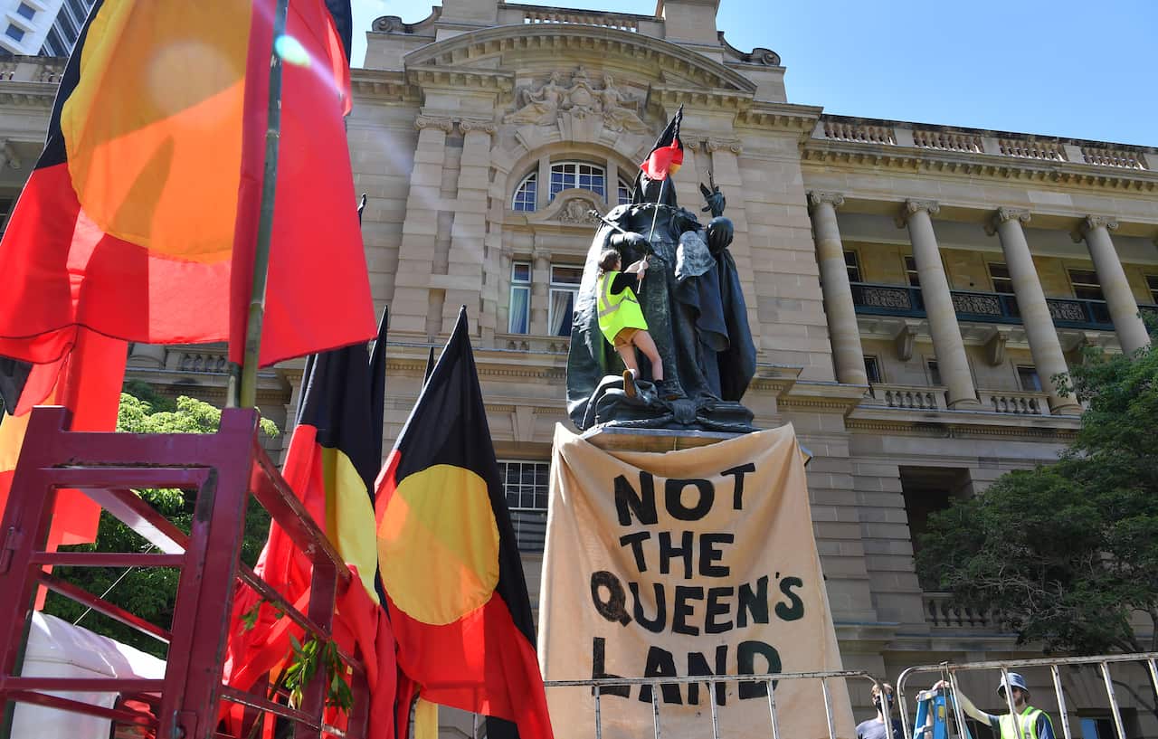 A protestor is seen attaching an Aboriginal flag to a statue of Queen Victoria in Brisbane's Queens Gardens.