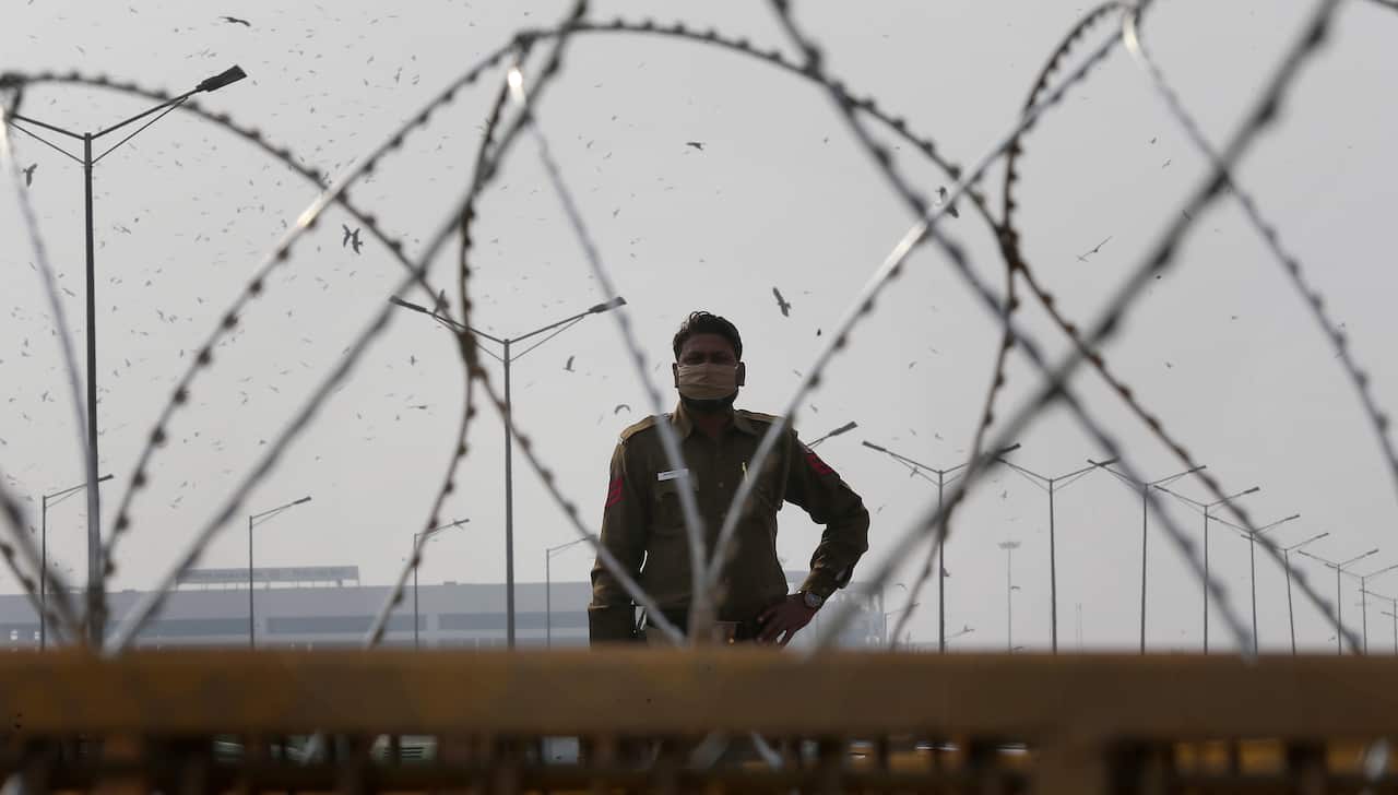 A policeman stands behind barbed wire and barricades placed by security personnel as farmers protest at the Delhi Ghazipur Border on 3 February.