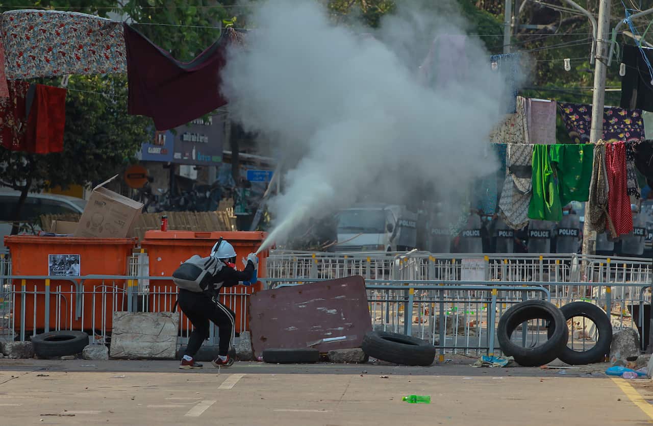 An anti-coup protester uses a fire extinguisher behind a line of women's clothing hung across a road to deter security personnel.