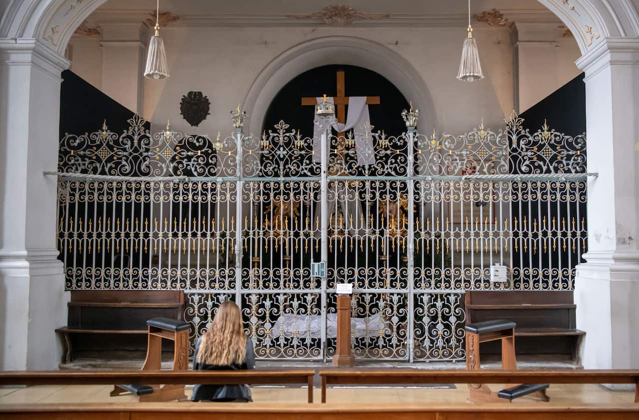02 April 2021, Bavaria, Munich: A woman sits in front of the closed Holy Sepulchre of the Church of the Holy Spirit on Good Friday. Photo: Peter Kneffel/dpa