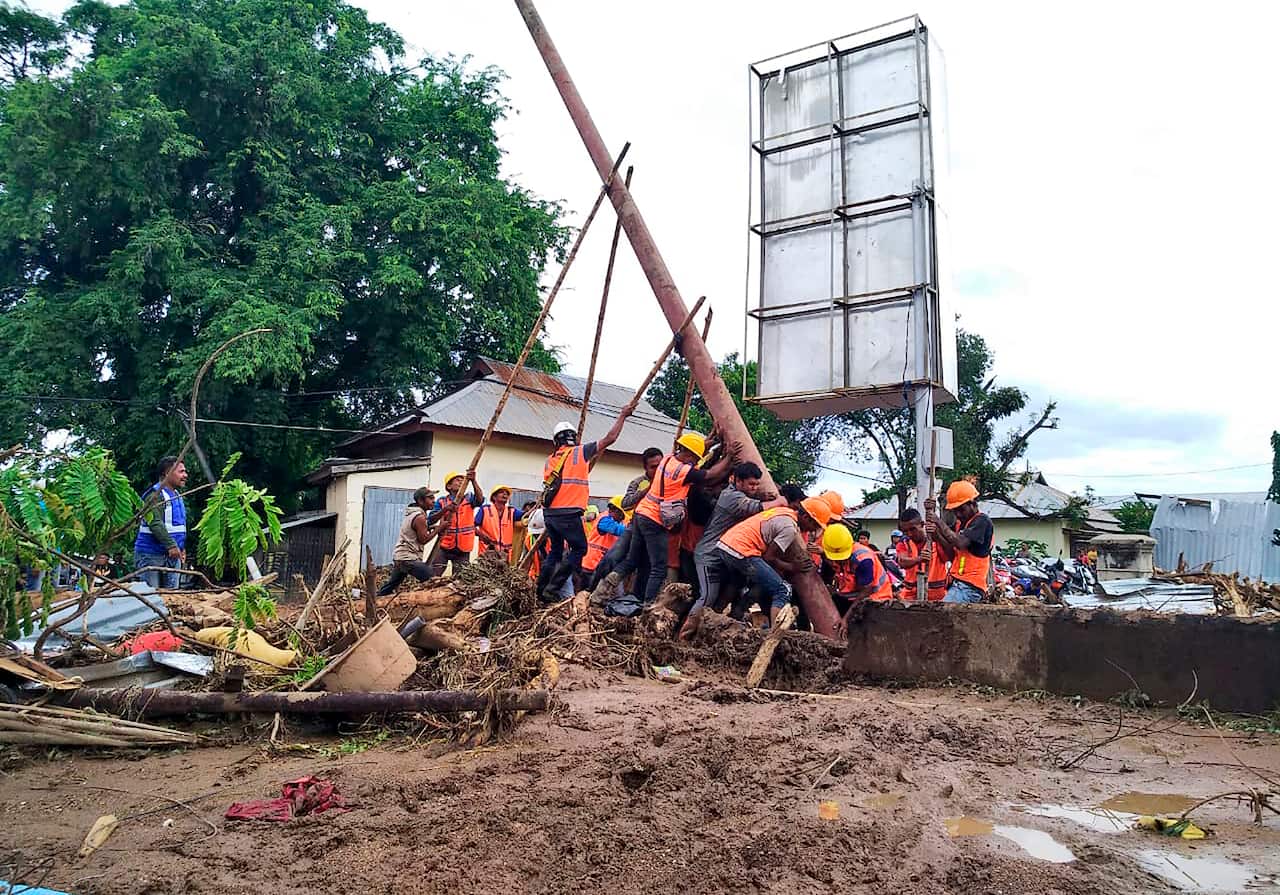 Workers erect an electricity pole to bring the power back on at a flood affected area in Waiwerang