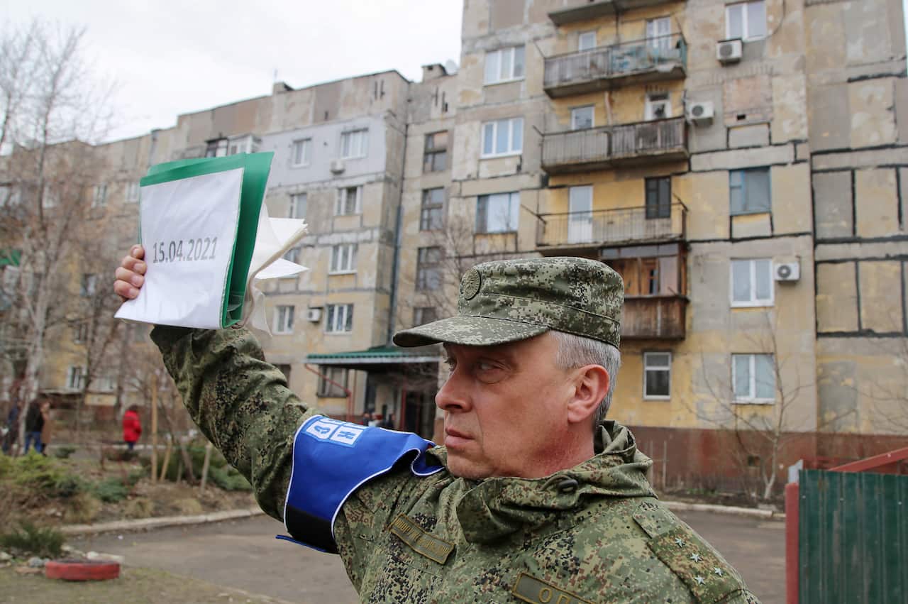 A representative of the Joint Center for Control and Coordination on ceasefire holds a sign by a house damaged in a shelling attack in Donetskt, Ukraine.