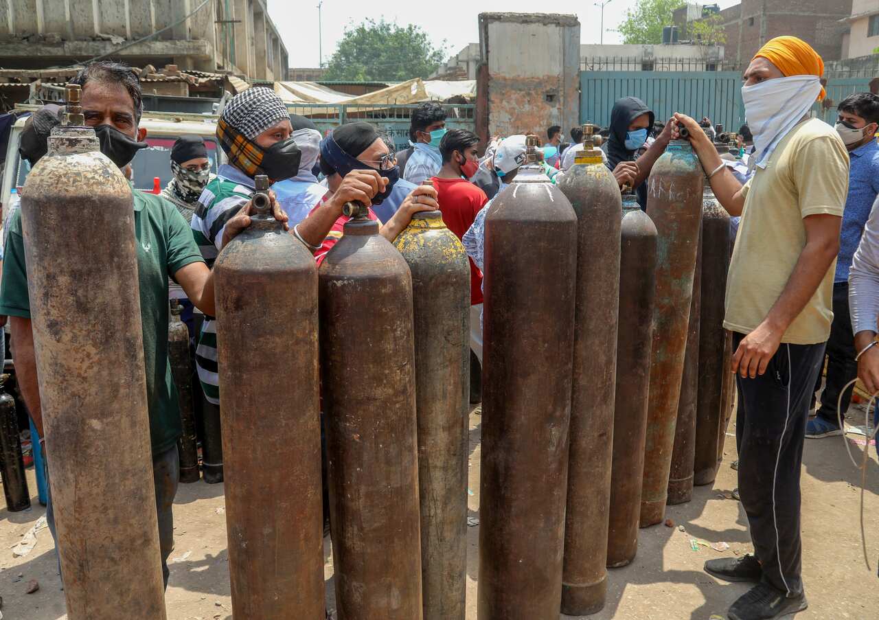 Family members of COVID-19 patients hold empty oxygen cylinders for refilling at Narayana Industrial area in New Delhi. 