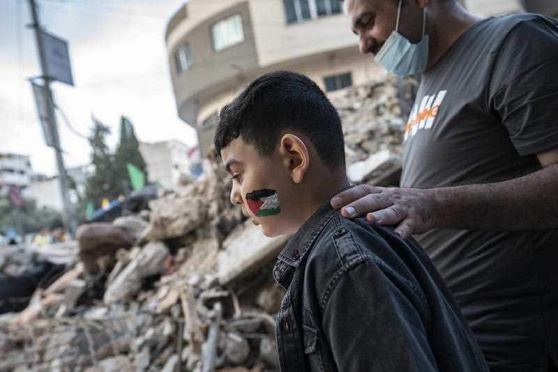 A child with a Palestinian flag painted on their face is led past a rubble heap beside a building previously destroyed by an air-strike in Gaza, 21 May, 2021. 