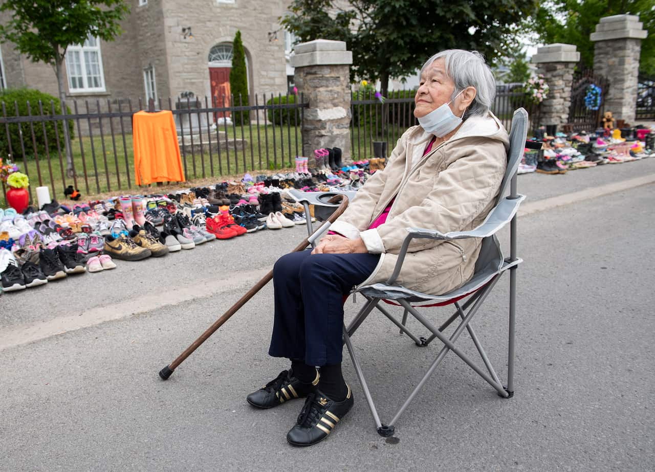 Residential school survivor Betty Deer sits next to children's shoes, placed outside a church in Quebec as a tribute to the victims of residential schools.
