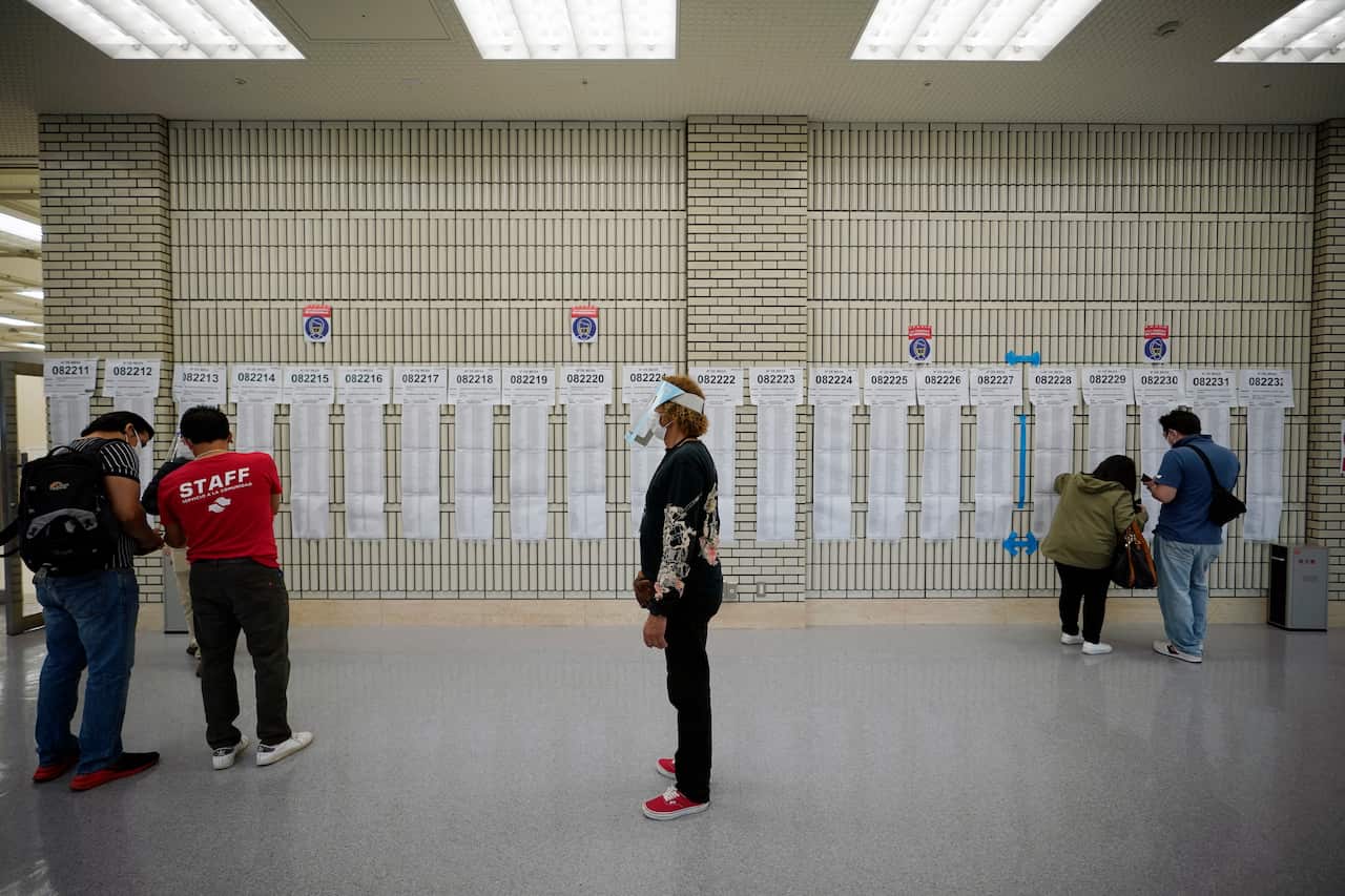 A staff member stands as Peruvian nationals living in Japan search their names on voters lists at a polling station in Tokyo, Japan, 6 June 2021. 