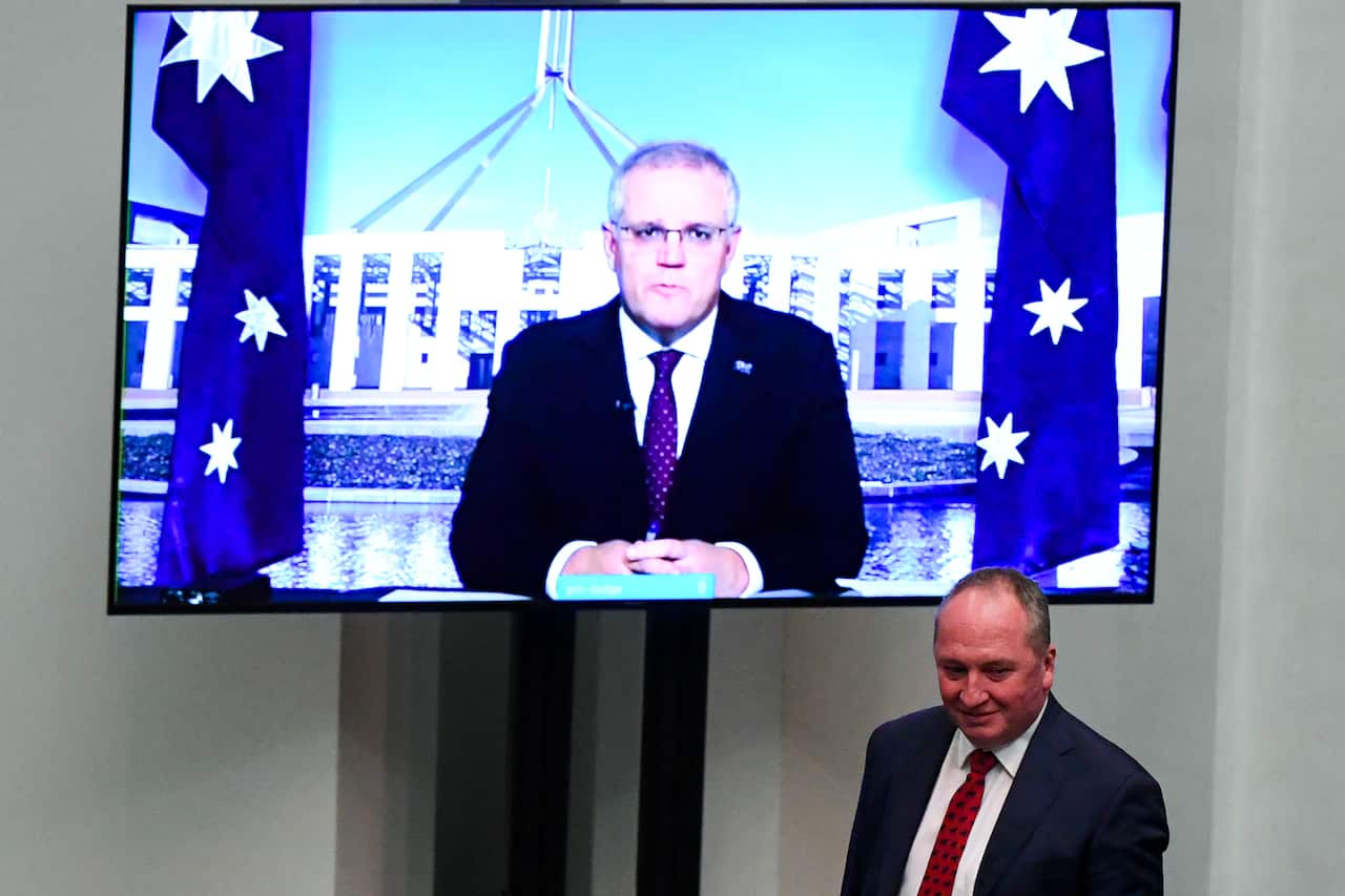 Newly-elected Nationals leader Barnaby Joyce walks past a screen showing Australian Prime Minister Scott Morrison.