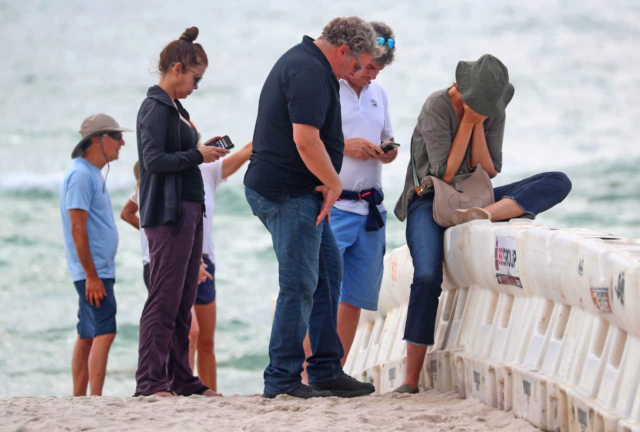 Mourners gather on the beach near the site of the 12-story oceanfront Champlain Towers South Condo that partially collapsed.