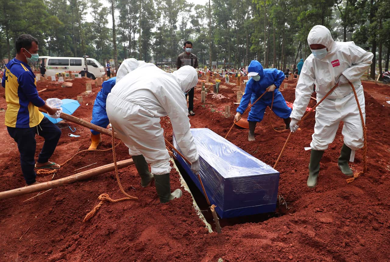 Workers in protective suits carry a coffin containing the body of a COVID-19 victim for a burial at a cemetery in Bogor, West Java, Indonesia, on 14 July, 2021.