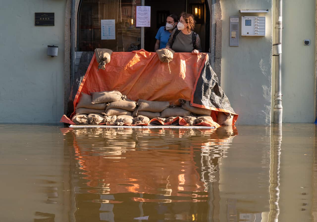 Two people look out of the entrance of a hotel over the flood barrier that is supposed to protect the building.