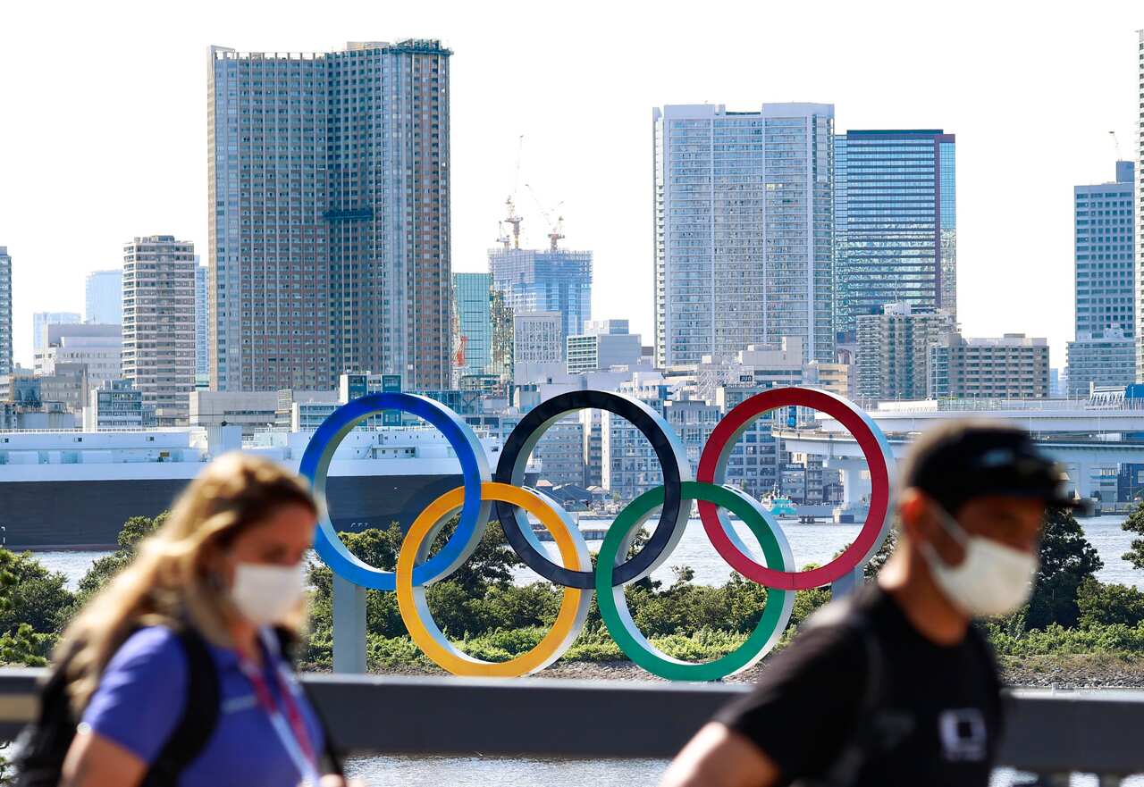 People wearing face masks amid the coronavirus pandemic pass by an Olympics rings monument in Tokyo.