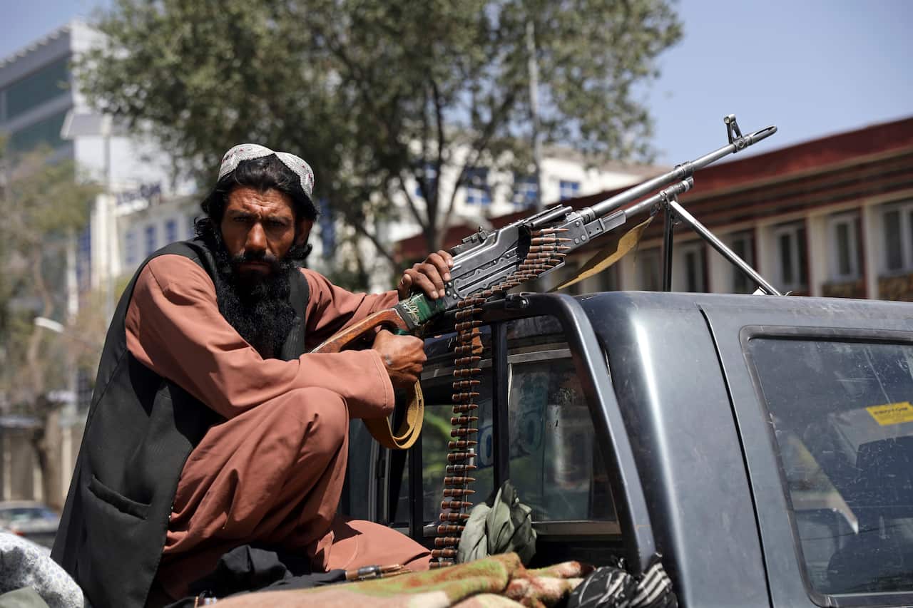 A Taliban fighter sits on the back of vehicle with a PK machine gun in front of the main gate leading to the Afghan presidential palace in Kabul