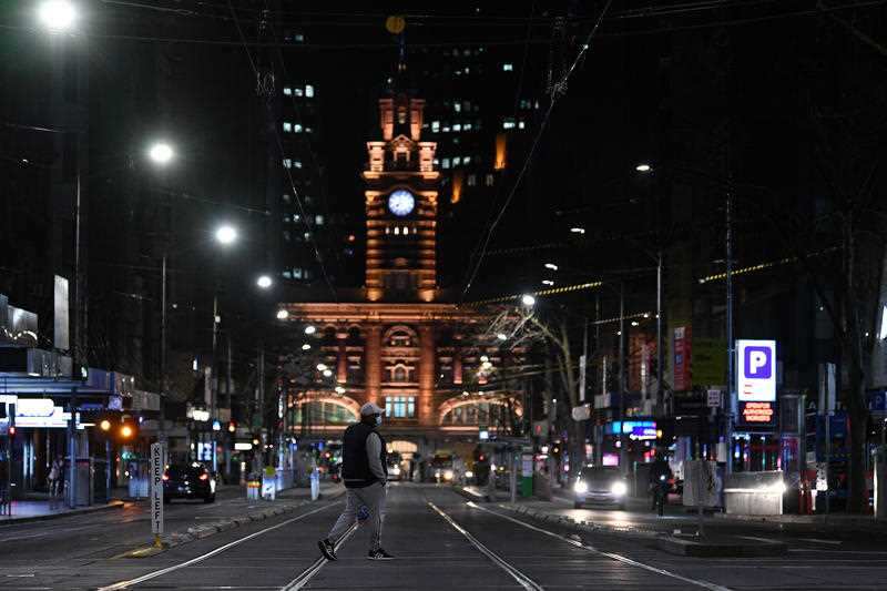A person wearing a face mask is seen crossing a street ahead of the curfew in Melbourne, Monday, 16 August, 2021.