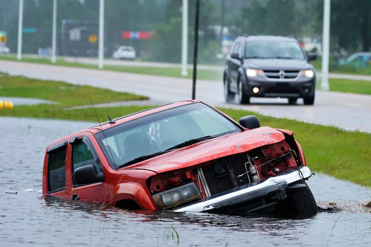 An abandoned vehicle half-submerged in a ditch next to a near flooded highway as the outer bands of Hurricane Ida arrive