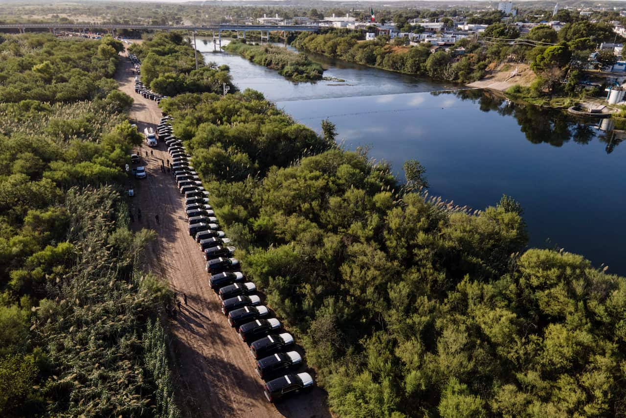 A line of Texas Department of Safety vehicles line up on the Texas side of the Rio Grande near the migrant camp