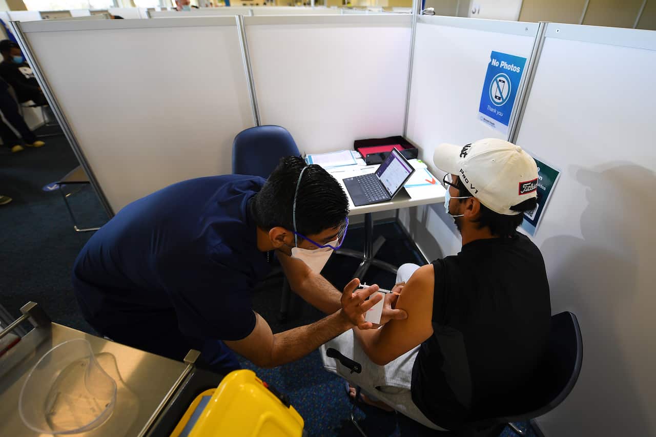 Khoa Nguyen (right) receives his Covid19 vaccination administered by a healthcare worker at the vaccination centre at Sandown Racecourse in Melbourne, Thursday, October 14, 2021. Victoria is on the brink of recording more than 2000 daily coronavirus infec